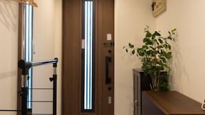 A hallway with a wooden door, a plant, a bench, and a shoe rack with shoes. - East Shinagawa Apartment (Tokyo)