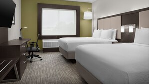 A hotel room with two beds, a desk, a chair, a TV, and a window.
