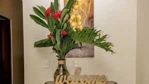 Et trækommode med et 'welcome' skilt, en vase med blomster og et billede på væggen.