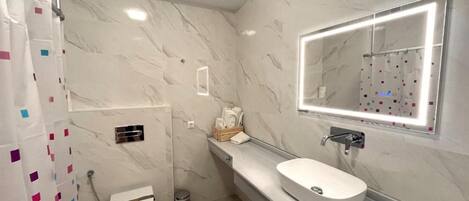 A modern bathroom with a marble wall, a white sink, and a mirror with lights.