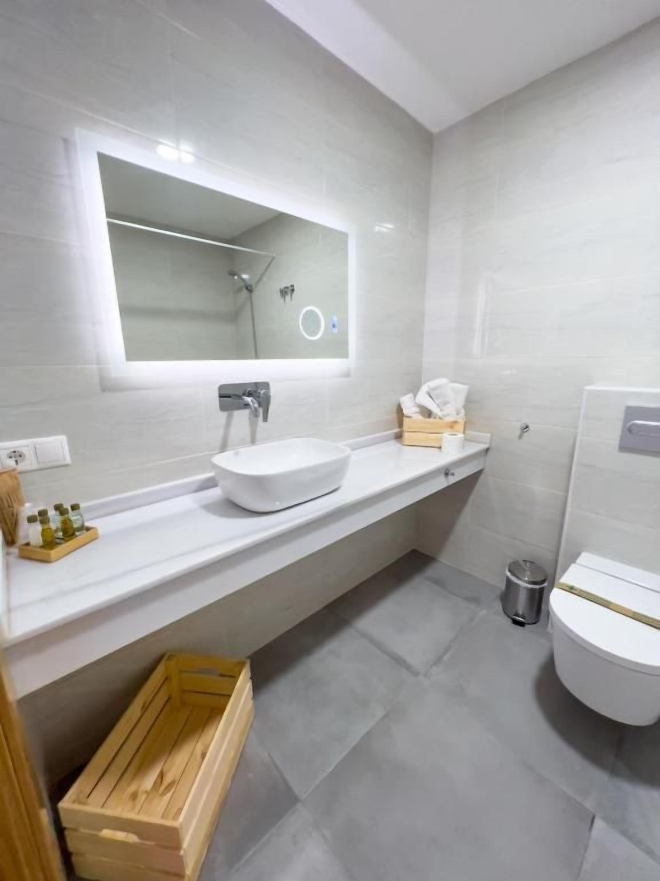 Un baño moderno con un espejo grande, un lavamanos blanco y un inodoro.