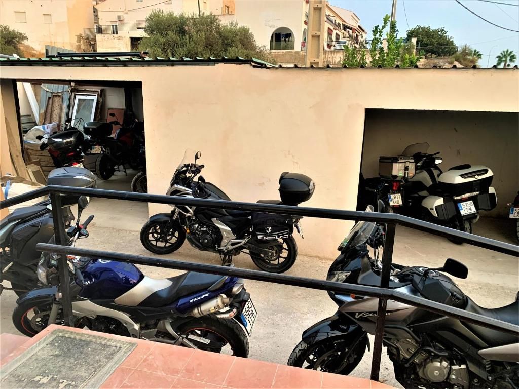 Une rangée de motos garées dans un parking couvert, avec un mur de couleur beige et une rambarde en métal.