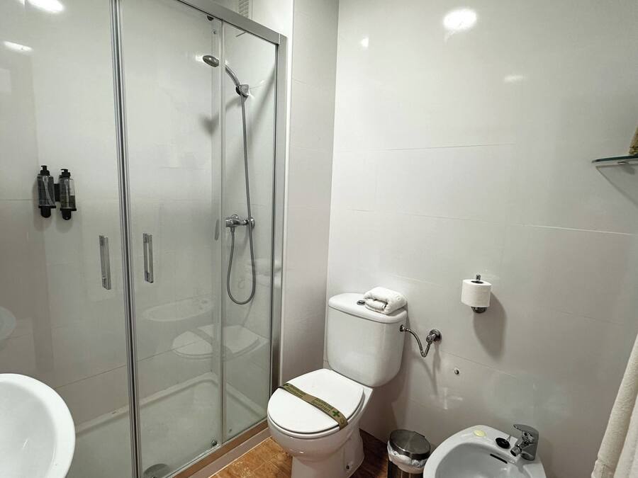 A modern bathroom with a glass-enclosed shower, a toilet with a paper towel dispenser, a sink with a soap dish, and a towel rack.