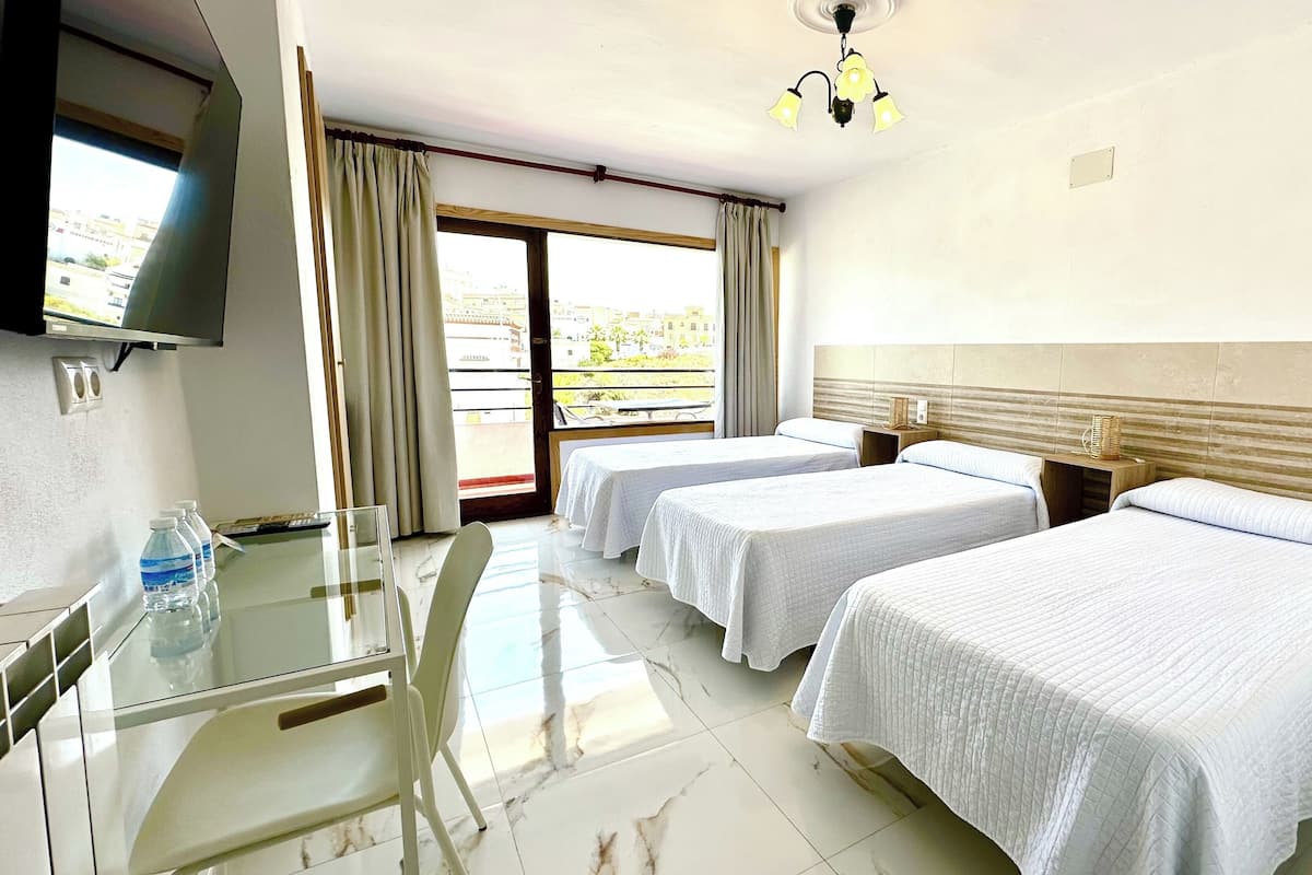 Habitación de hotel con dos camas, televisión, una mesa de vidrio y balcón con cortinas.