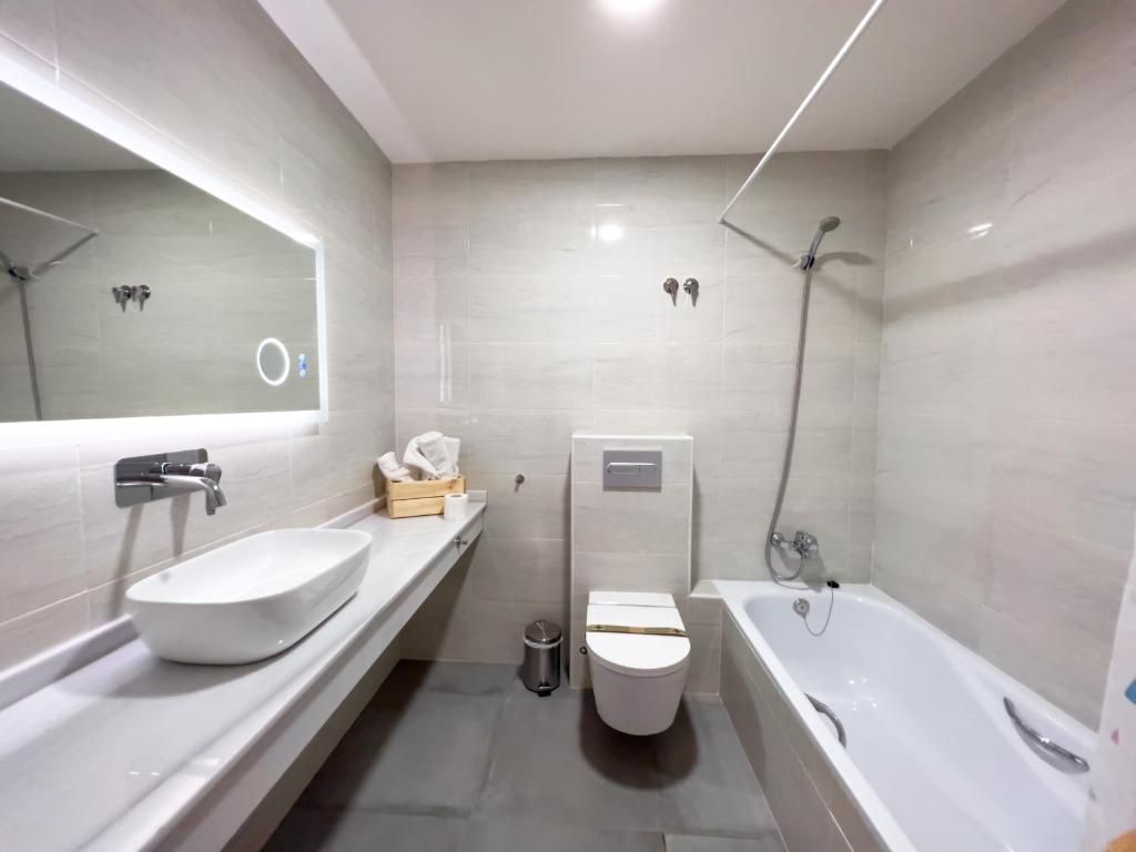 Ein modernes Badezimmer mit einem großen Spiegel, einem weißen Waschbecken, einer Toilette und einer Badewanne.