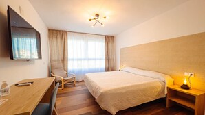 A hotel room with a bed, a desk, a chair, a TV, and a window with curtains. - Hostal Sorbas (Sorbas)