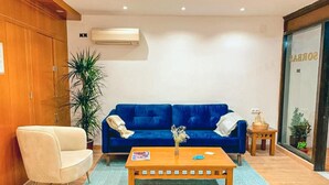 A living room with a blue sofa, a wooden coffee table, a cream-colored armchair, and a small side table with a basket. - Hostal Sorbas (Sorbas)