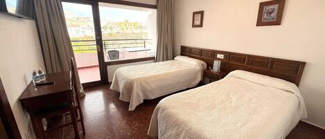A hotel room with two beds, a desk, a chair, a small table, and a balcony with a view.