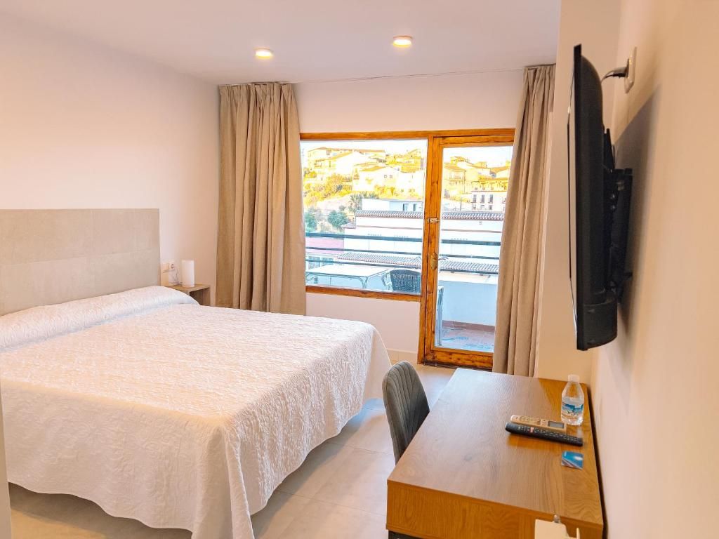 Une chambre d’hôtel avec un lit, un bureau, une télévision et une fenêtre avec des rideaux.