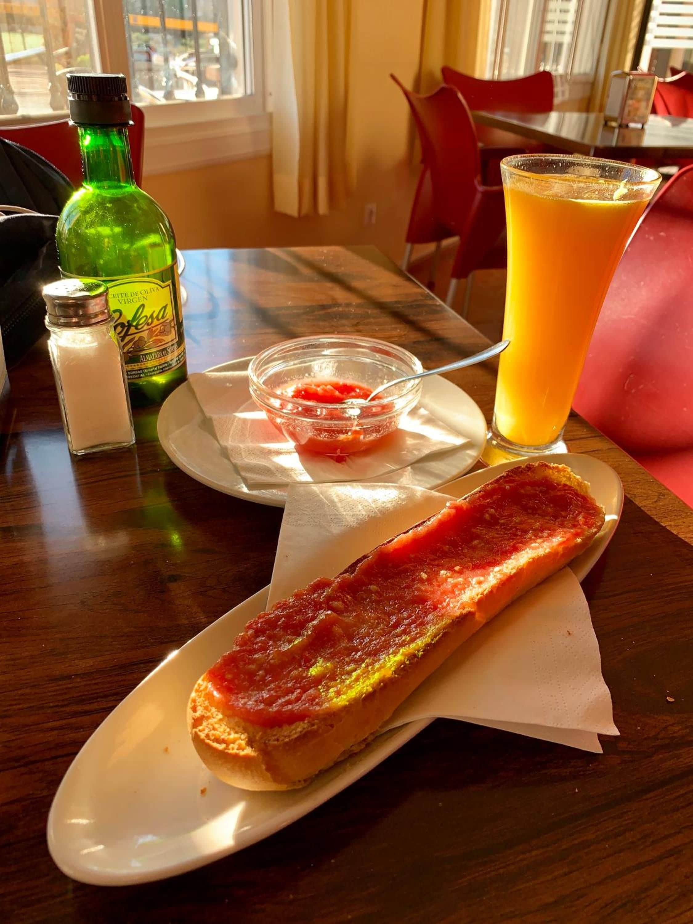 Ateria, johon kuuluu bruschetta-leipää, lasi appelsiinimehua ja pullo oliiviöljyä, ja kaikki on tarjoiltu puupöydällä.