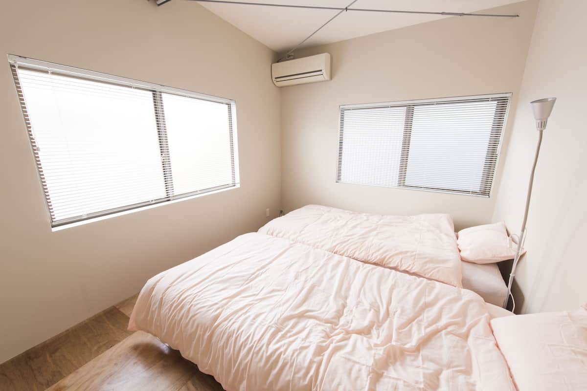 A bedroom with a bed, two windows, an air conditioner, and a floor lamp.