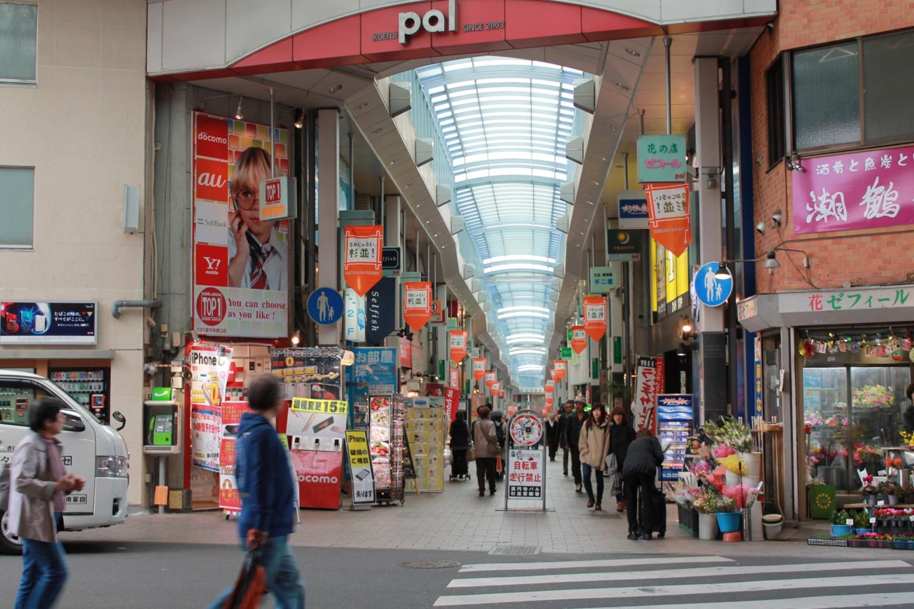 Una zona comercial concurrida, varios comercios y un paso de peatones.