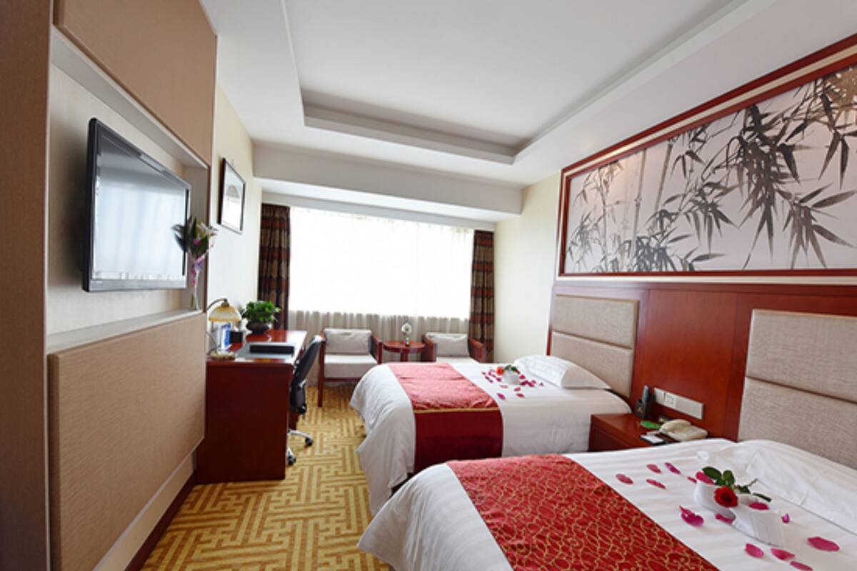 Une chambre d’hôtel avec deux lits, un bureau, une chaise, une télévision et un grand tableau au mur.