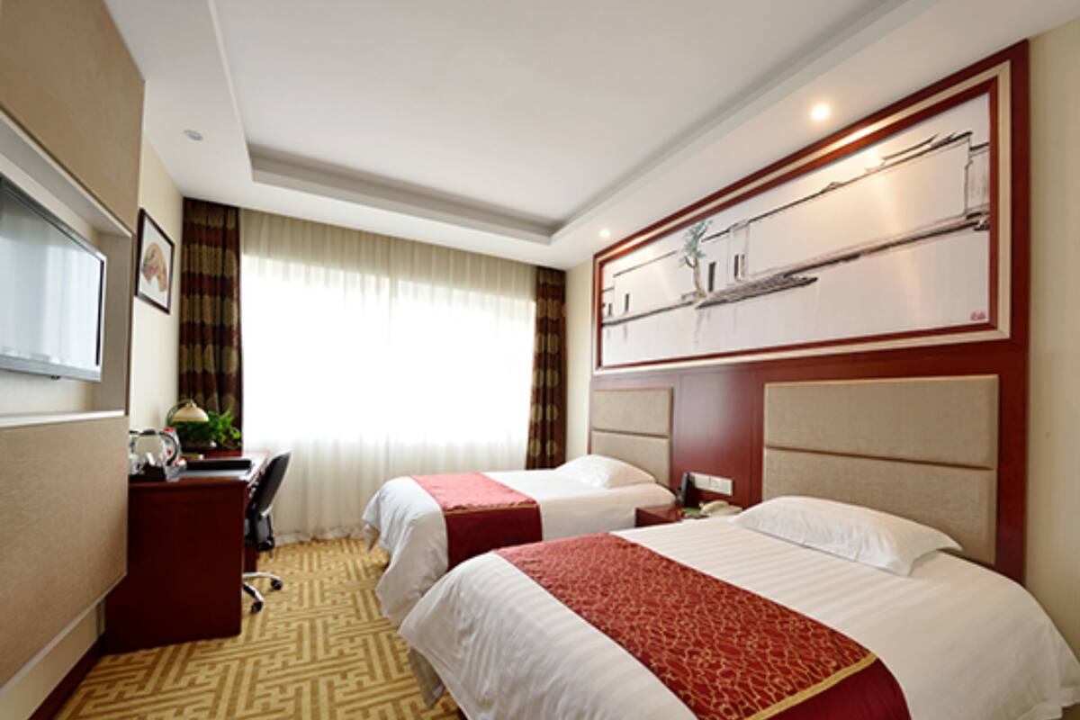 Une chambre d’hôtel avec deux lits, un bureau, une chaise, une télévision et une fenêtre avec des rideaux.