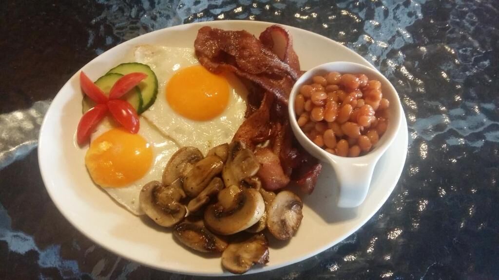 A plate with eggs, bacon, mushrooms, beans, and vegetables.