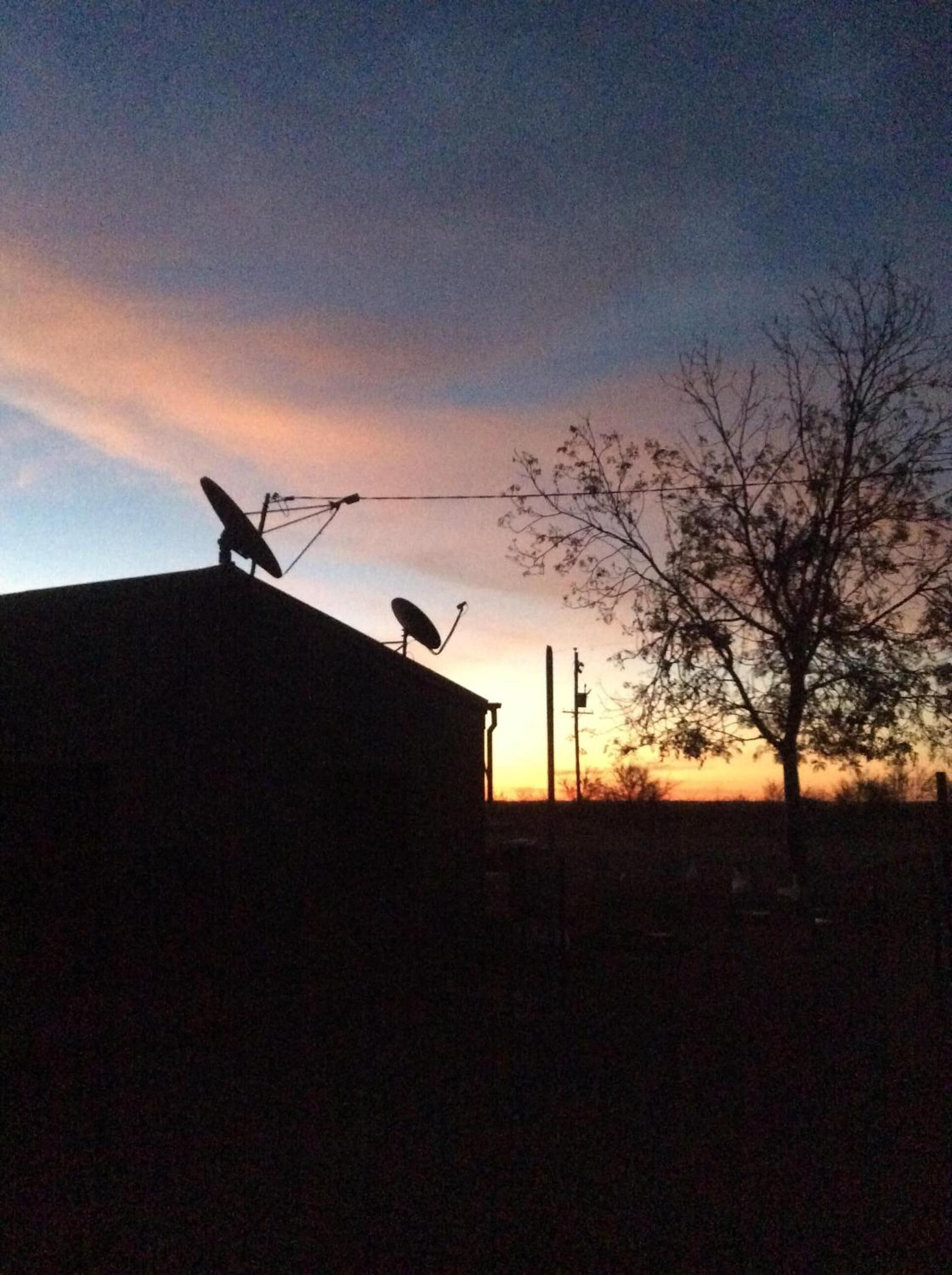 A building with satellite dishes on the roof, surrounded by trees and a sunset sky.