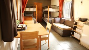 A compact room with bunk beds, a sofa, a dining table, and a kitchenette.