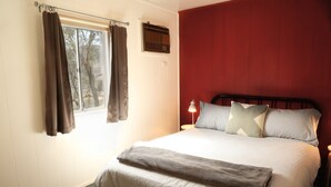 A bedroom with a bed, curtains, a nightstand, a lamp, and a wall-mounted heater.