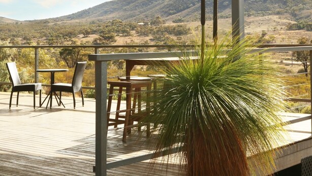 A covered outdoor area with a table and chairs, overlooking a hilly landscape.