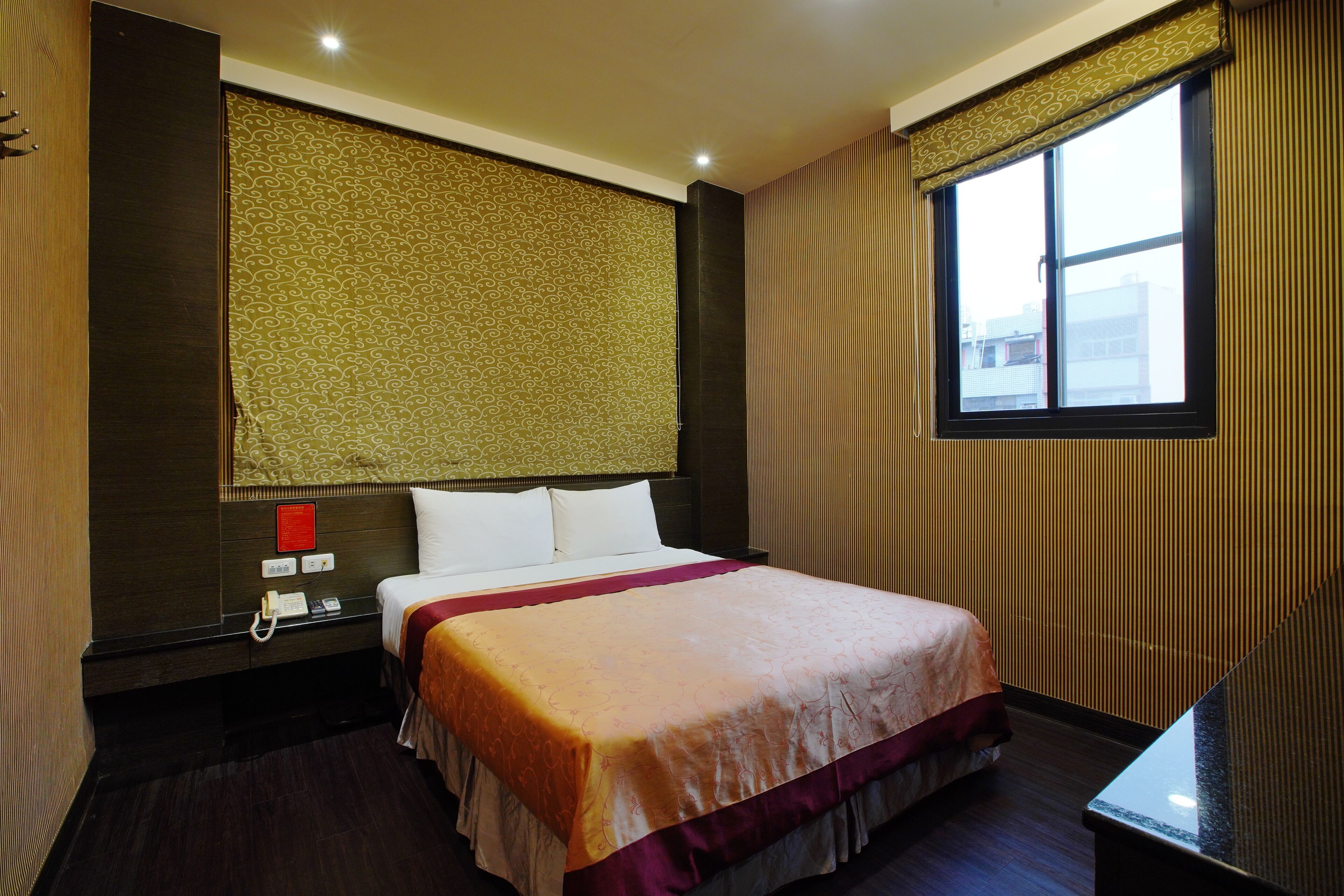 Una habitación de hotel con una cama grande, una mesita de noche, un teléfono y una ventana con cortinas.