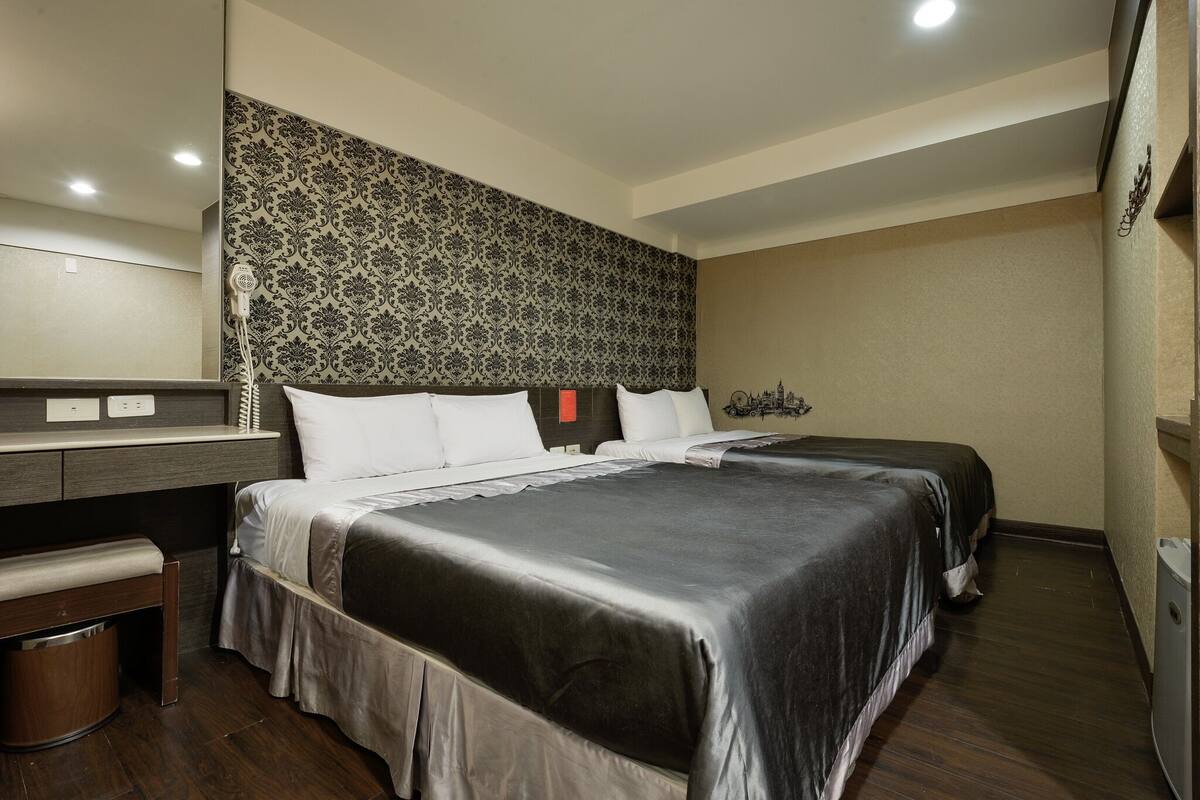 Una habitación de hotel con dos camas, un escritorio, una silla y un espejo grande.