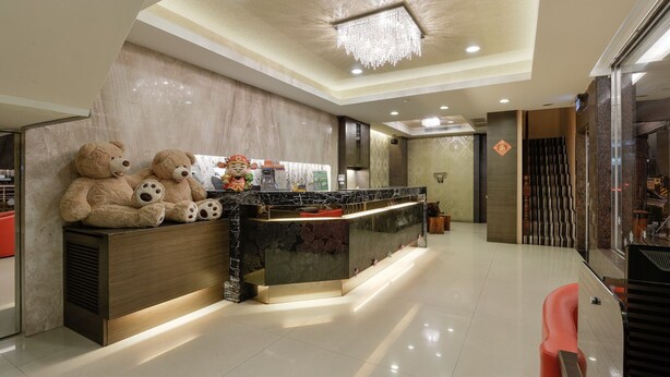 Zona de recepción de un hotel con mostrador de mármol, adorables osos de peluche y una lámpara de araña moderna.