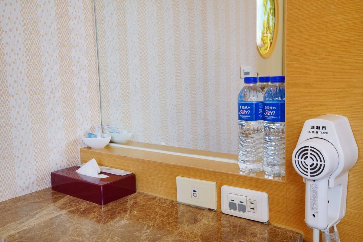 Un baño de hotel con espejo, caja de pañuelos, secador de pelo y botellas de agua.