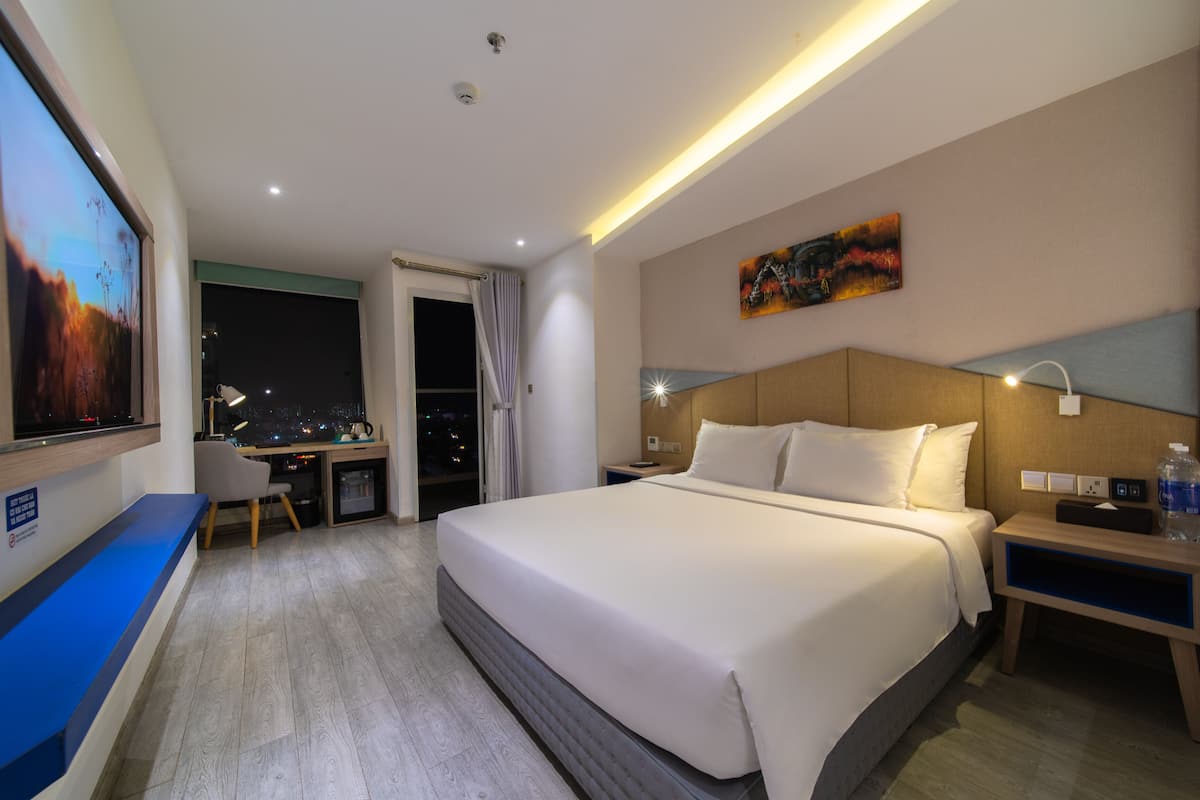 A hotel room with a large bed, a desk with a chair, a TV, and a painting on the wall.