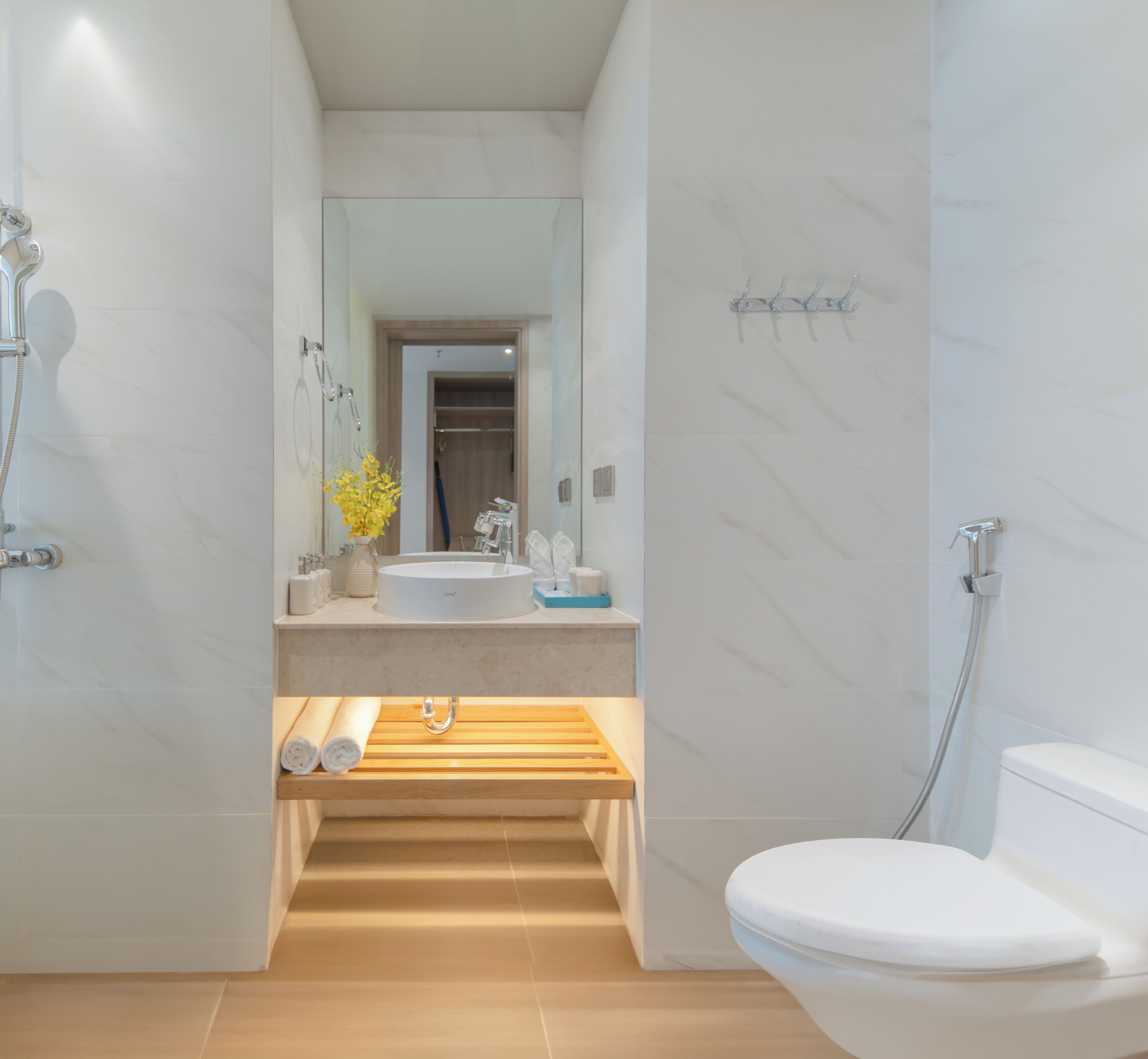 Un baño moderno con inodoro blanco, lavamanos con espejo y zona de ducha con cabezal de ducha de mano.