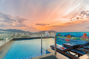 A rooftop infinity pool with a view of the city and mountains, a mural of an underwater scene, and lounge chairs. - Le's Cham Hotel (Nha Trang)