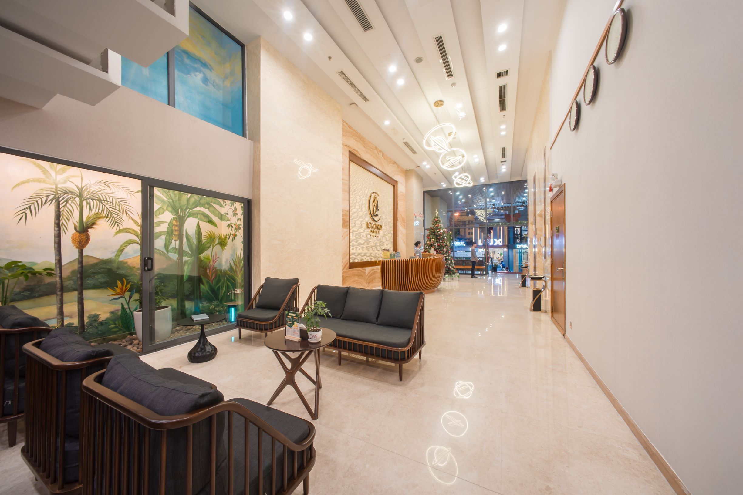 A modern lobby with seating areas, a reception desk, and a large window with tropical artwork.