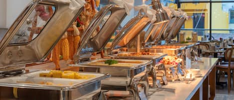 Montaje tipo buffet con múltiples estaciones de autoservicio, incluyendo bandejas para diversos alimentos y una decoración con mazorcas de maíz.