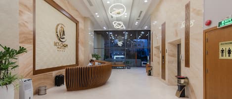 A hotel reception area with a curved reception desk, a large logo on the wall, and a sign indicating a restroom.