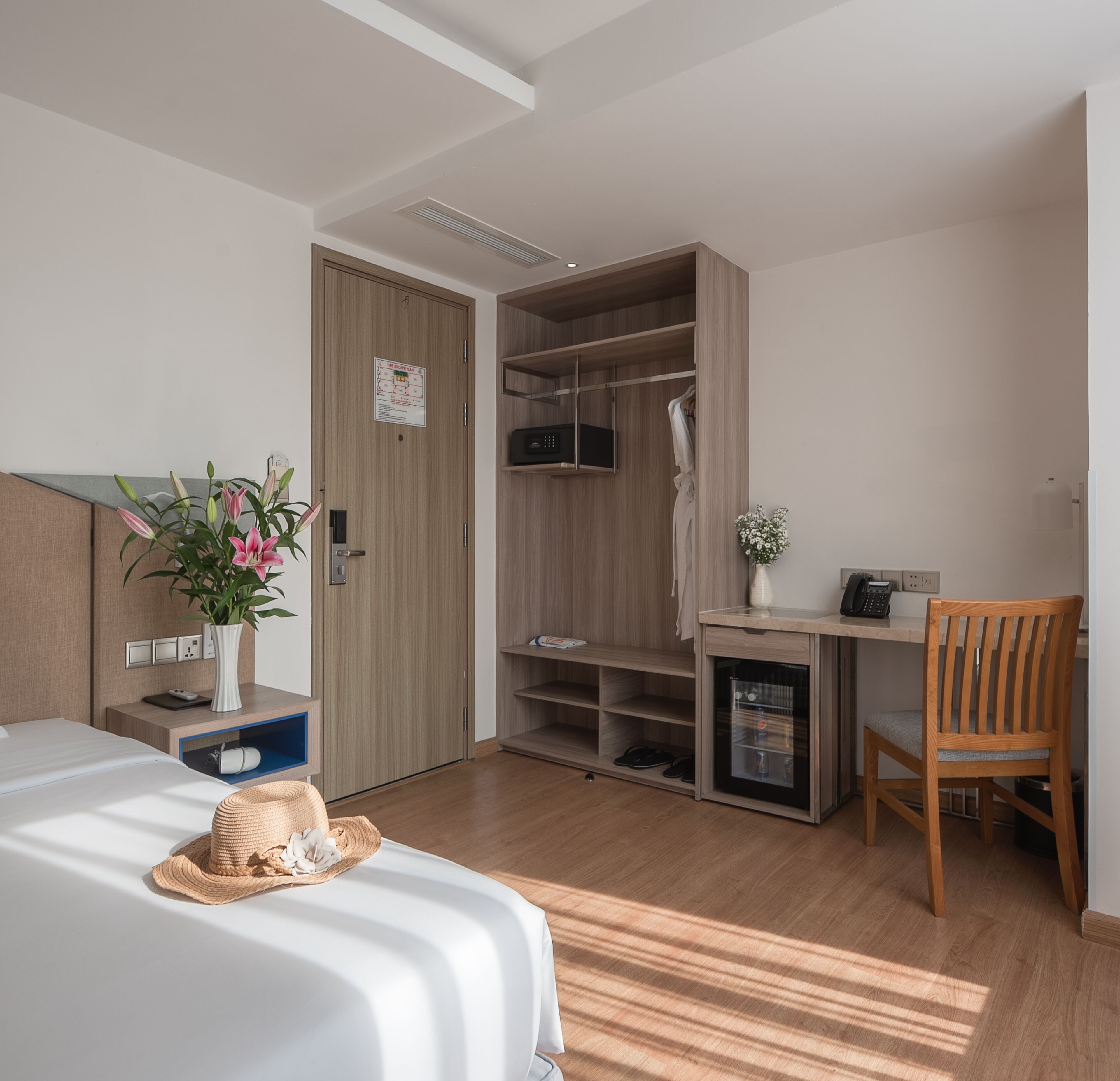 A modern hotel room with a bed, a desk, a wardrobe, and a small kitchenette.
