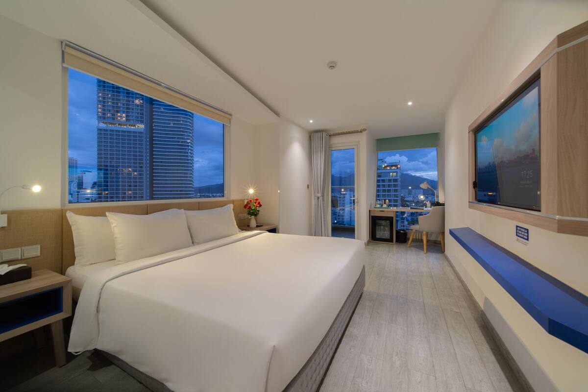 A hotel room with a large bed, a desk, and a view of the cityscape.
