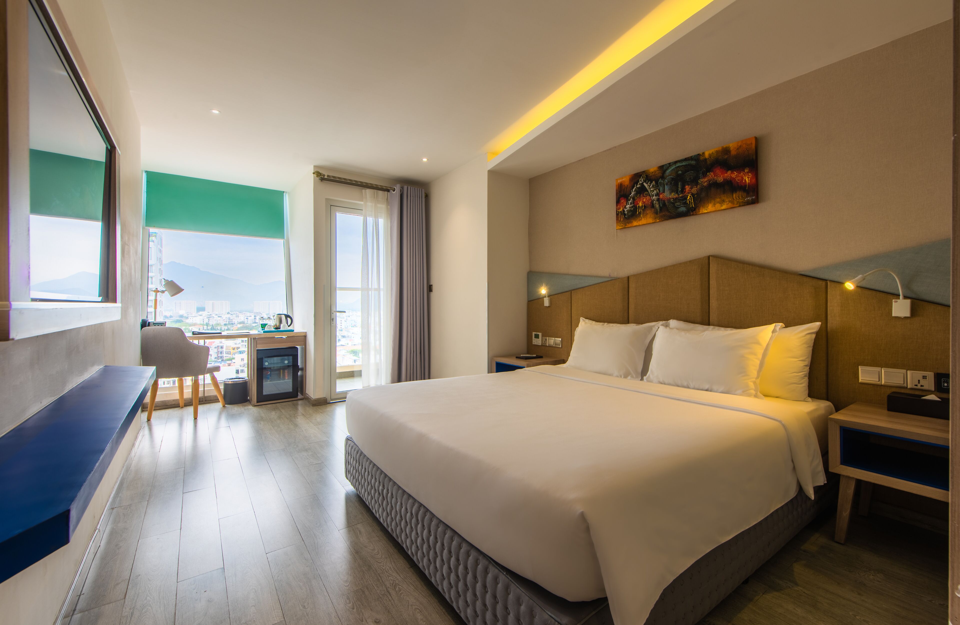 A hotel room with a large bed, a desk, and a view of the city.