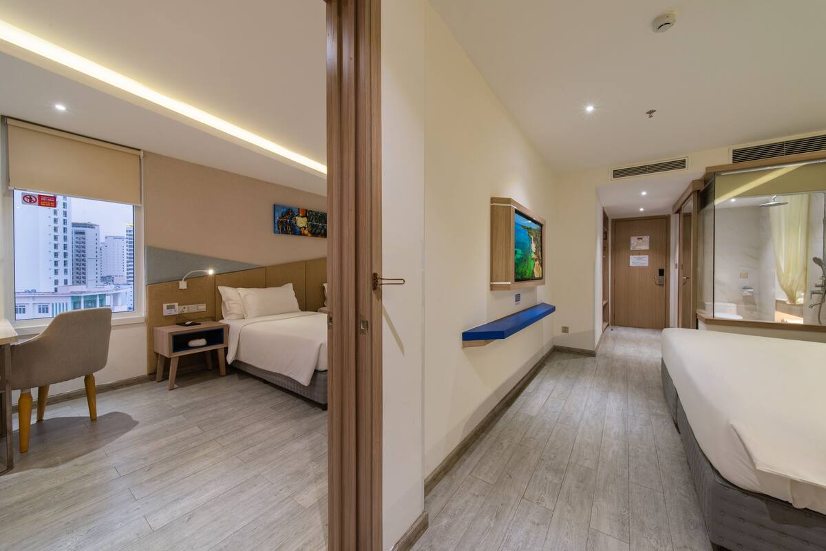 A hotel room with a bed, a desk, a chair, a nightstand, a TV, and a window with a city view.