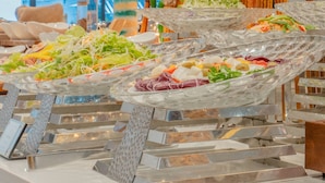 Un bufé con diversos platos, incluyendo ensaladas y carnes, dispuesto sobre una mesa de vidrio.