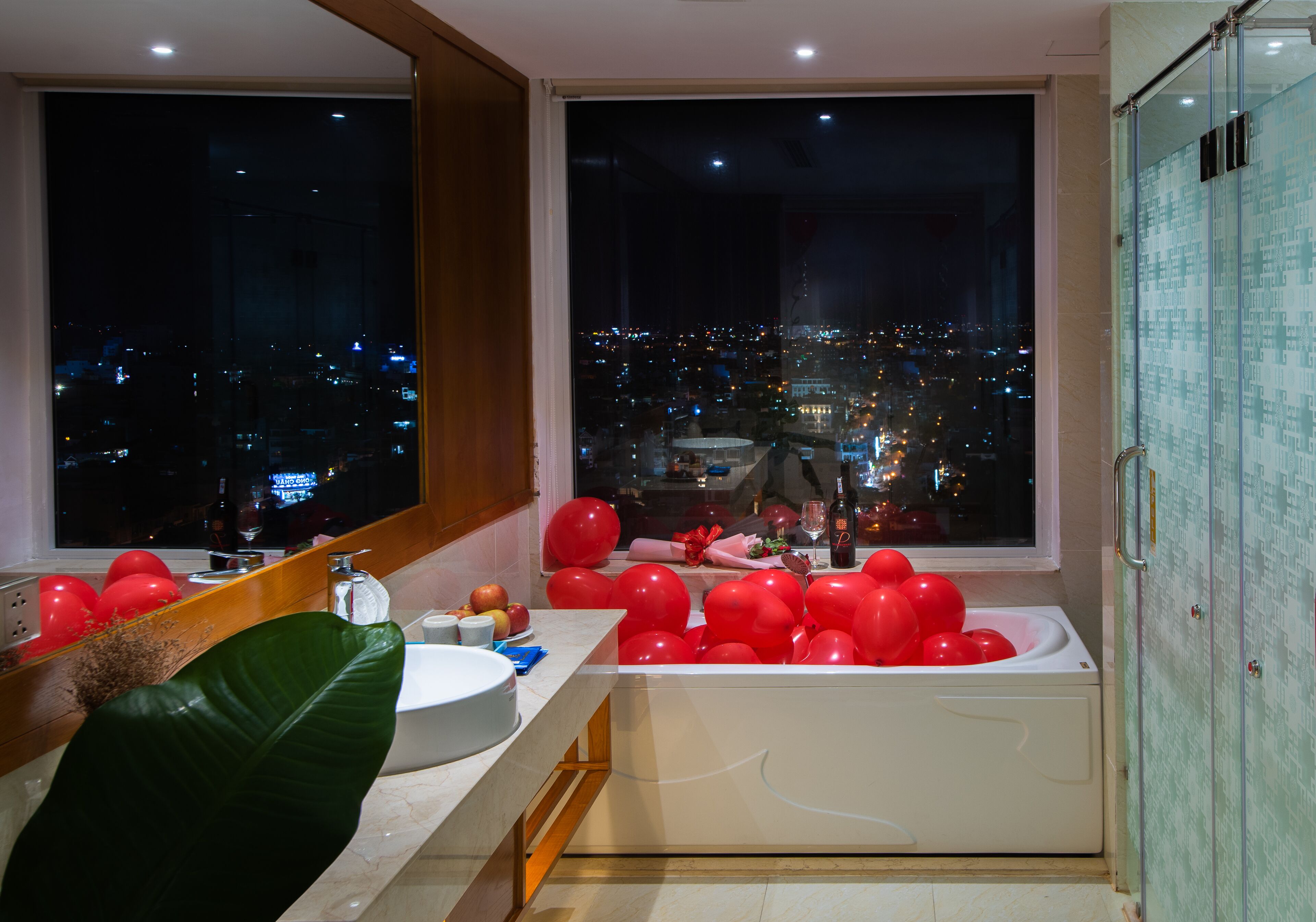 Een moderne badkamer met een bad, een grote spiegel en uitzicht op een stadsbeeld 's nachts.