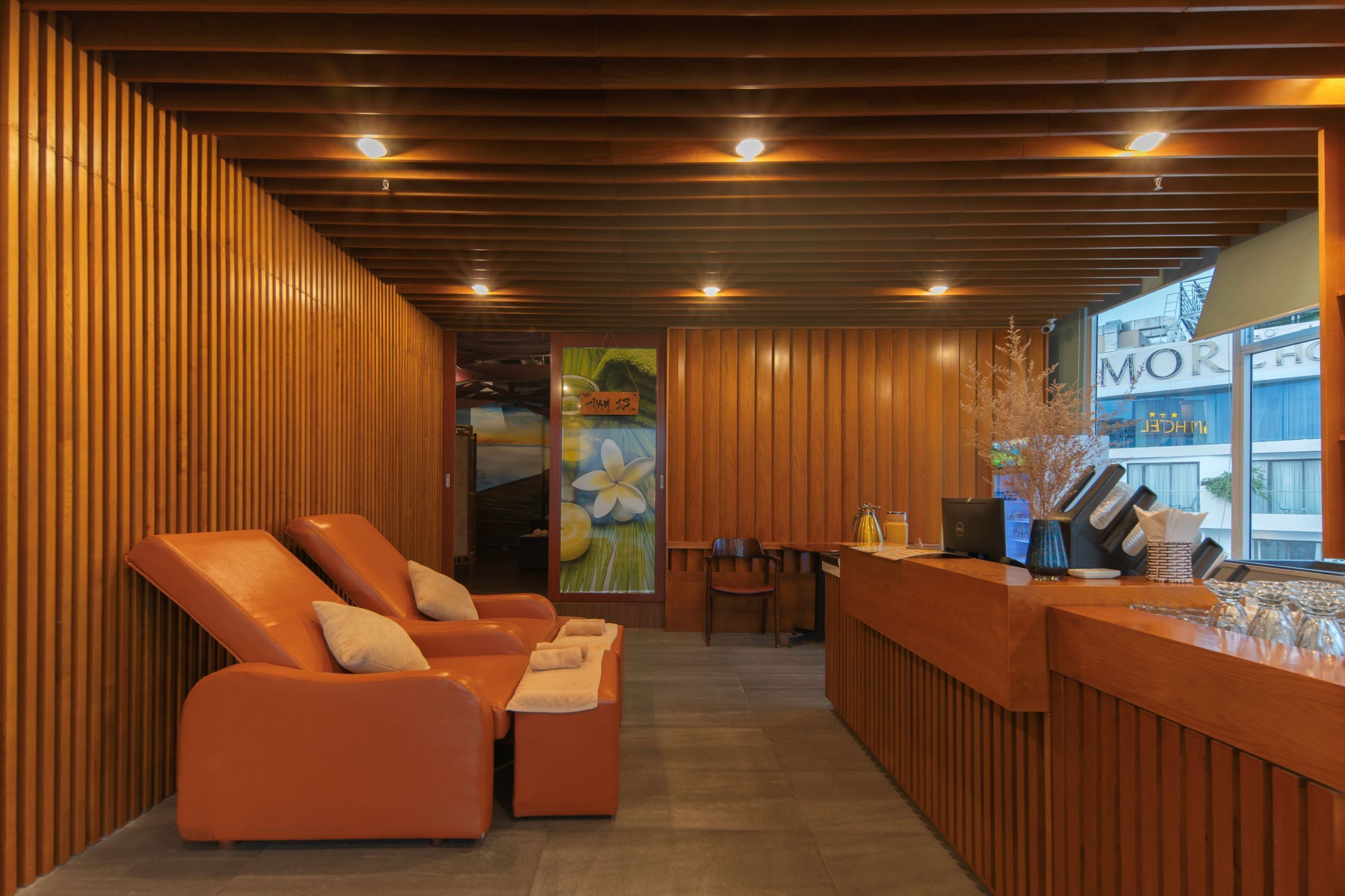 A reception area with wooden paneling, a reception desk, two orange lounge chairs, and a view of the outside.