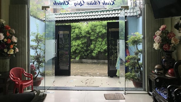 A traditional Thai gate with a sign above it, leading to a courtyard with potted plants and a red chair.