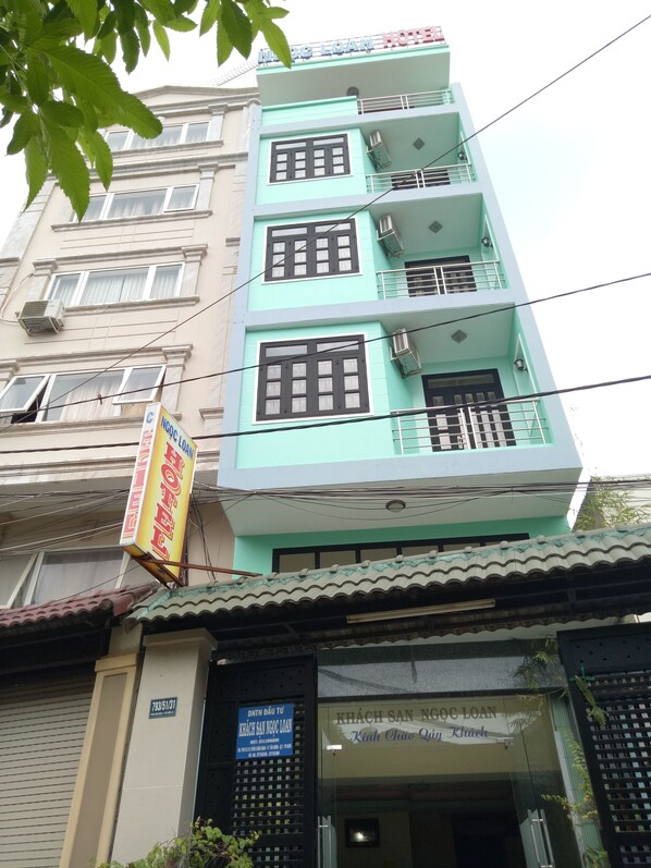A multi-story building with a light blue facade, multiple balconies, and a sign indicating it is a hotel.