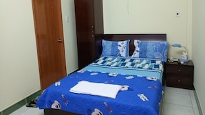 A bedroom with a bed, a wardrobe, a fan, and a nightstand with a lamp and a phone.