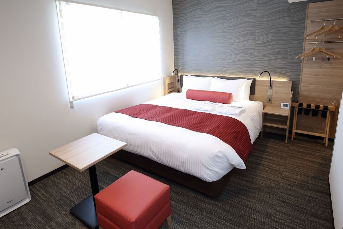 A hotel room with a bed, bedside table, and a small stool.