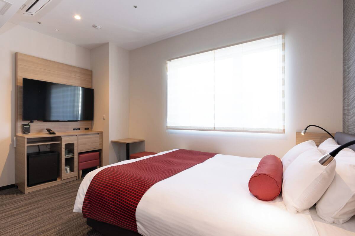 Una habitación de hotel con cama, televisión, escritorio y ventana.