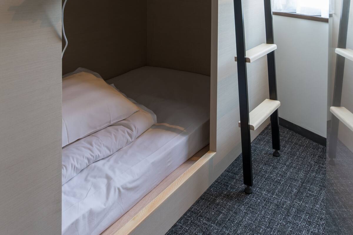 A bunk bed with a ladder, a desk, and a window with curtains.