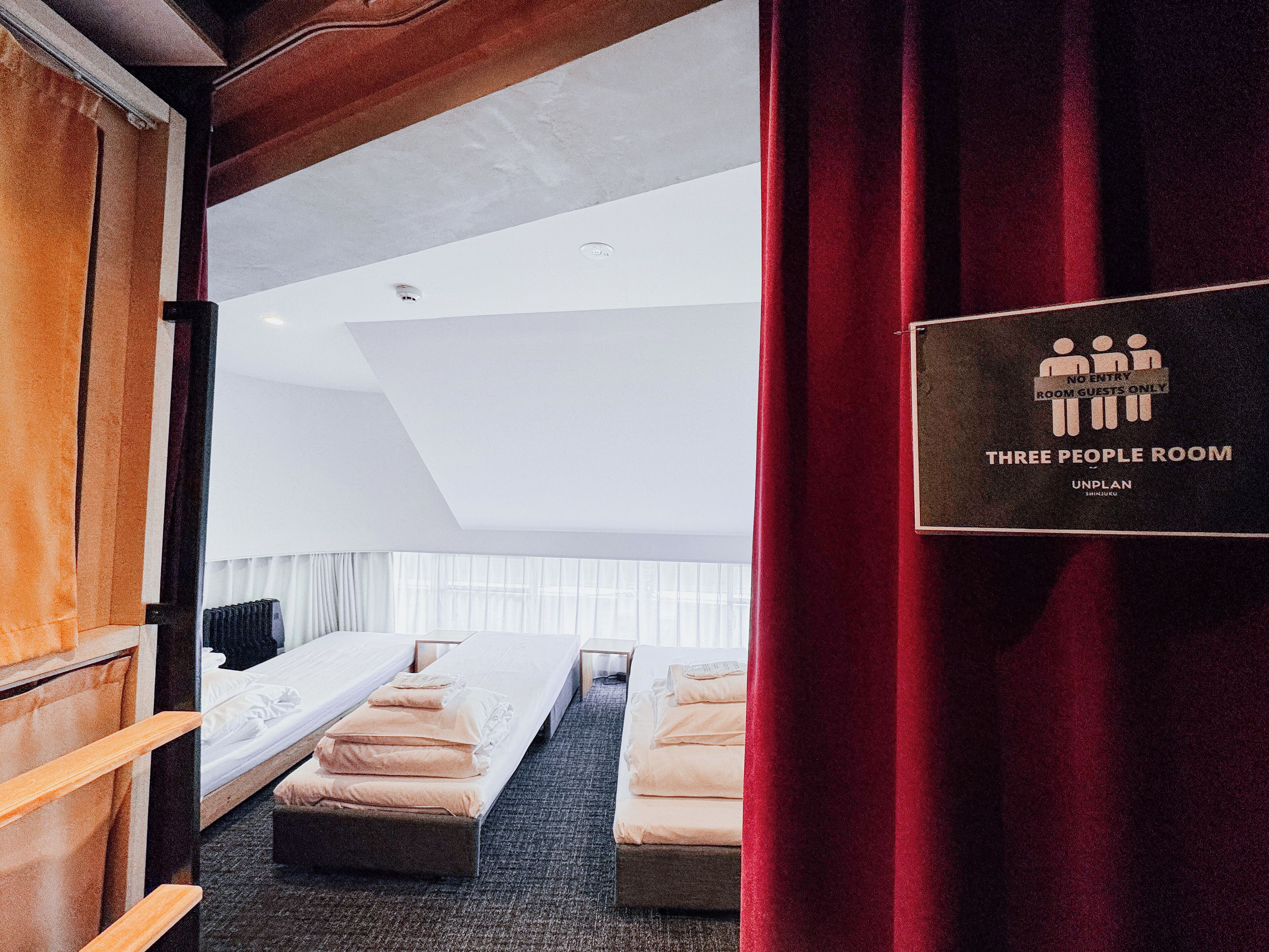 A three-person room with a bed, a desk, and a chair. There is a sign indicating it is a three-person room.