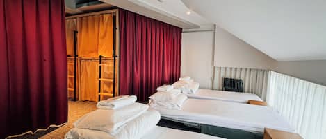 Hotellihuone, jossa on kaksi sänkyä, punaiset verhot, puinen tikapuut ja näkymä parvekkeelle.
