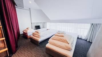 Une chambre d’hôtel avec deux lits, une grande fenêtre avec des rideaux légers, un rideau rouge sur le côté gauche et un sol recouvert de moquette.