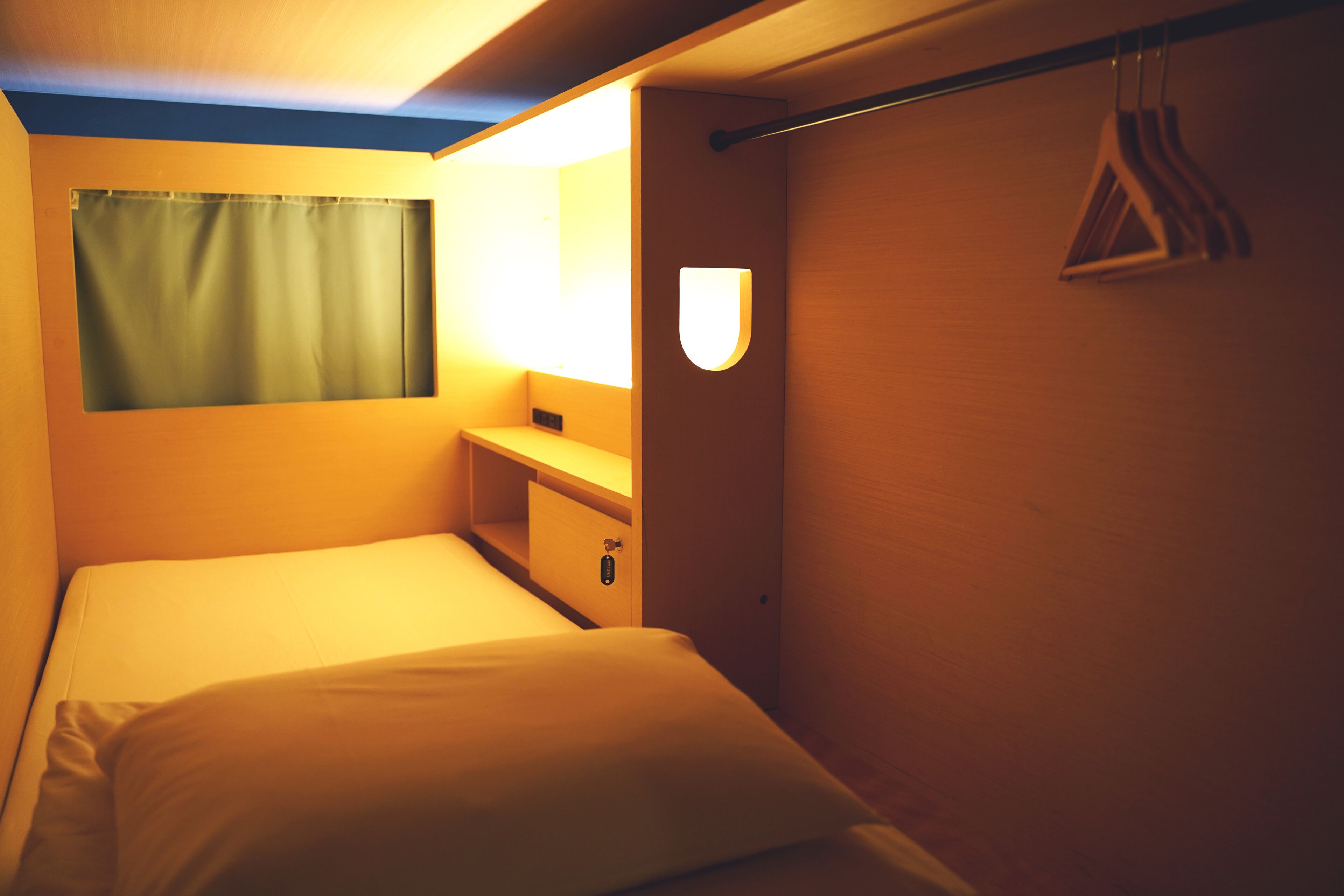 Een kleine hotelkamer met een eenpersoonsbed, een nachtkastje, een spiegel en een kapstok.